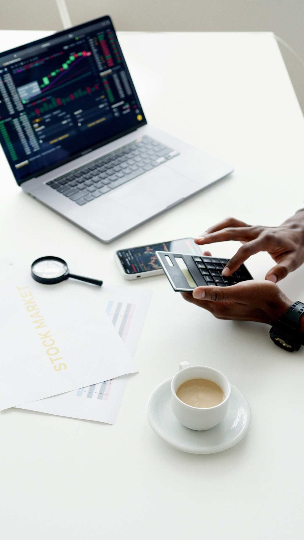 Image d'un homme sur son bureau avec un café, un ordinateur, une loupe et une calculatrice